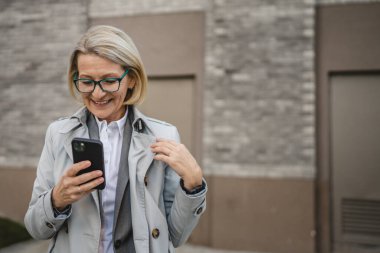 Modern bir kadın şehirde yetişkin bir kadın cep telefonu kullanıyor kısa mesajlar yolluyor ya da internete takılıyor gözlüklü sarışın bir kadın.