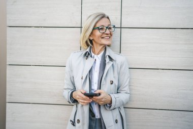 Modern bir kadın şehirde yetişkin bir kadın cep telefonu kullanıyor kısa mesajlar yolluyor ya da internete takılıyor gözlüklü sarışın bir kadın.