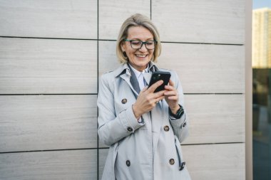 Modern bir kadın şehirde yetişkin bir kadın cep telefonu kullanıyor kısa mesajlar yolluyor ya da internete takılıyor gözlüklü sarışın bir kadın.