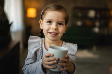 Küçük bir kız çocuğu, beyaz çocuk elinde bir bardak su tutuyor.