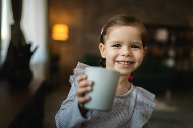Küçük bir kız çocuğu, beyaz çocuk elinde bir bardak su tutuyor.