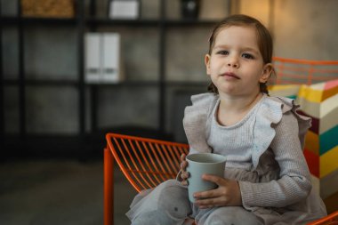 Küçük bir kız çocuğu, beyaz çocuk elinde bir bardak su tutuyor.