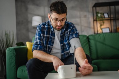 Man caucasian male sit at the table at home check measure blood pressure real person health care concept