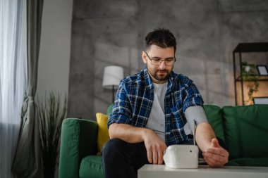 Man caucasian male sit at the table at home check measure blood pressure real person health care concept