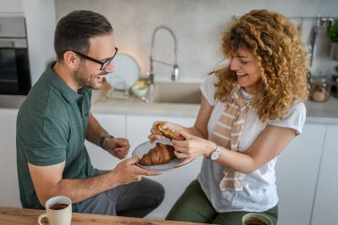 Kafkasyalı çift mutfakta kahvaltı yapıyor. Günlük kruvasan ve kahve yiyor. Sıradan bir aile hayatı.
