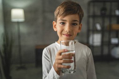 Beyaz tenli bir çocuk, elinde bir bardak su, önünde içki, beyaz gömlek, fotokopi makinesi, mutlu bir gülümseme.