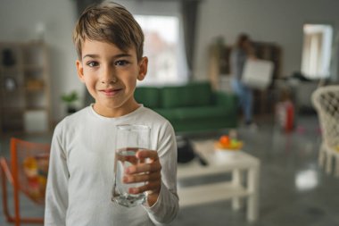 Beyaz tenli bir çocuk, elinde bir bardak su, önünde içki, beyaz gömlek, fotokopi makinesi, mutlu bir gülümseme.
