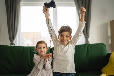 İki çocuk, küçük beyaz erkek ve kız kardeş mutlu çocuklar erkek ve kız kardeşler oyun konsolu oyunu oynarken evde otururken oyun konsolu ya da kumanda ile gerçek insanlar gerçek aile eğlencesi konsepti