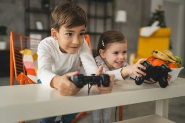 İki çocuk, küçük beyaz erkek ve kız kardeş mutlu çocuklar erkek ve kız kardeşler oyun konsolu oyunu oynarken evde otururken oyun konsolu ya da kumanda ile gerçek insanlar gerçek aile eğlencesi konsepti