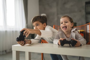İki çocuk, küçük beyaz erkek ve kız kardeş mutlu çocuklar erkek ve kız kardeşler oyun konsolu oyunu oynarken evde otururken oyun konsolu ya da kumanda ile gerçek insanlar gerçek aile eğlencesi konsepti