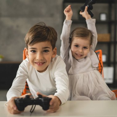 İki çocuk, küçük beyaz erkek ve kız kardeş mutlu çocuklar erkek ve kız kardeşler oyun konsolu oyunu oynarken evde otururken oyun konsolu ya da kumanda ile gerçek insanlar gerçek aile eğlencesi konsepti