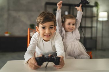 İki çocuk, küçük beyaz erkek ve kız kardeş mutlu çocuklar erkek ve kız kardeşler oyun konsolu oyunu oynarken evde otururken oyun konsolu ya da kumanda ile gerçek insanlar gerçek aile eğlencesi konsepti