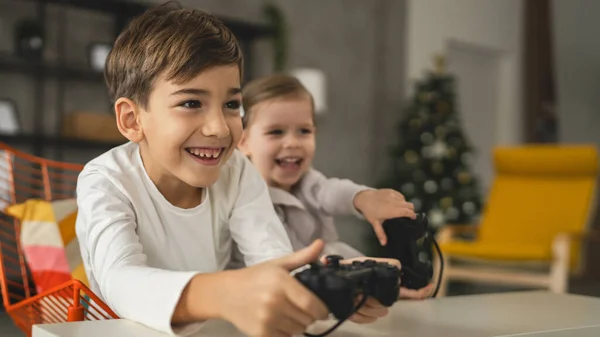 两个孩子小高加索兄弟姐妹快乐的孩子兄弟姐妹男孩和女孩坐在家里玩电玩控制台的时候用控制杆或控制器真人家庭休闲的概念 — 图库照片