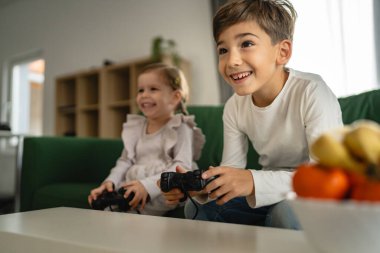 İki çocuk, küçük beyaz erkek ve kız kardeş mutlu çocuklar erkek ve kız kardeşler oyun konsolu oyunu oynarken evde otururken oyun konsolu ya da kumanda ile gerçek insanlar gerçek aile eğlencesi konsepti