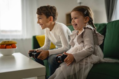 İki çocuk, küçük beyaz erkek ve kız kardeş mutlu çocuklar erkek ve kız kardeşler oyun konsolu oyunu oynarken evde otururken oyun konsolu ya da kumanda ile gerçek insanlar gerçek aile eğlencesi konsepti