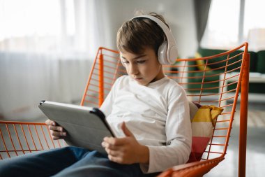 Bir beyaz çocuk evde oturup dijital tablet kullanıyor.