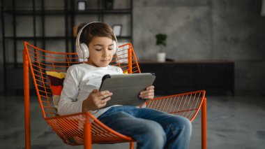 Bir beyaz çocuk evde oturup dijital tablet kullanıyor.