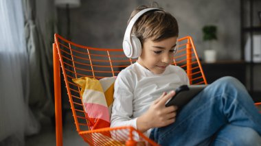 Bir beyaz çocuk evde oturup dijital tablet kullanıyor.
