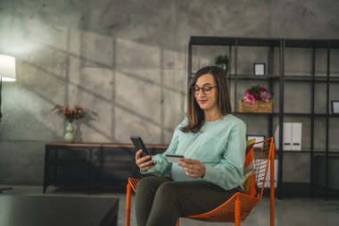 Hamile bir kadın online alışveriş yapıyor. Kredi kartı tutuyor. Evde oturuyor.