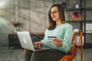 Hamile bir kadın online alışveriş yapıyor. Kredi kartı tutuyor. Evde oturuyor.
