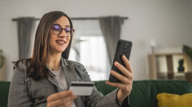 Hamile bir kadın online alışveriş yapıyor. Kredi kartı tutuyor. Evde oturuyor.