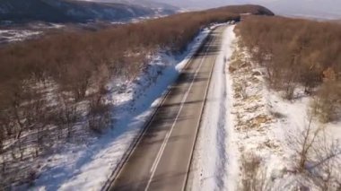 Minibüs kış günü kar altında dağ sırasındaki hava manzarasında yol alır.