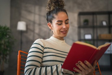 Genç bir yetişkin kadın. Bir kadın evde kitap okuyor ya da okuyor.