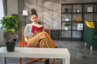 Genç bir yetişkin kadın. Bir kadın evde kitap okuyor ya da okuyor.