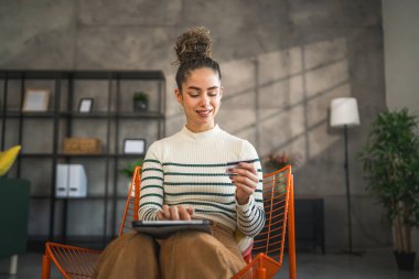 Yetişkin beyaz bir kadın mutlu bir şekilde gülümseyerek evde oturuyor banka kredi kartlarını online alışveriş konseptinde tutuyor gerçek insanlar uzay e-ticaretini kopyalıyor ya da rezervasyon yaptırıyor.