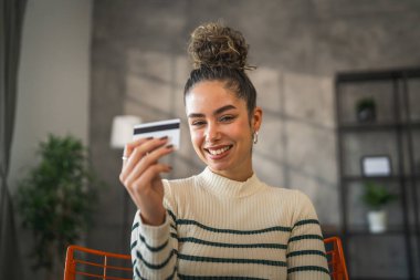 Yetişkin beyaz bir kadın mutlu bir şekilde gülümseyerek evde oturuyor banka kredi kartlarını online alışveriş konseptinde tutuyor gerçek insanlar uzay e-ticaretini kopyalıyor ya da rezervasyon yaptırıyor.