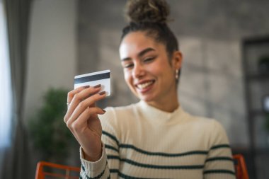 Yetişkin beyaz bir kadın mutlu bir şekilde gülümseyerek evde oturuyor banka kredi kartlarını online alışveriş konseptinde tutuyor gerçek insanlar uzay e-ticaretini kopyalıyor ya da rezervasyon yaptırıyor.