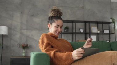 Yetişkin beyaz bir kadın mutlu bir şekilde gülümseyerek evde oturuyor banka kredi kartlarını online alışveriş konseptinde tutuyor gerçek insanlar uzay e-ticaretini kopyalıyor ya da rezervasyon yaptırıyor.