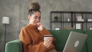 Yetişkin beyaz bir kadın mutlu bir şekilde gülümseyerek evde oturuyor banka kredi kartlarını online alışveriş konseptinde tutuyor gerçek insanlar uzay e-ticaretini kopyalıyor ya da rezervasyon yaptırıyor.