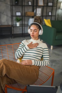 Yetişkin bir kadın Kafkas kadın milenyumu kulaklıkları online rehberli meditasyon için kullanıyor evde gözleri kapalı farkındalık yogası yapıyor gerçek insanların kişisel bakım kavramını taklit ediyor.