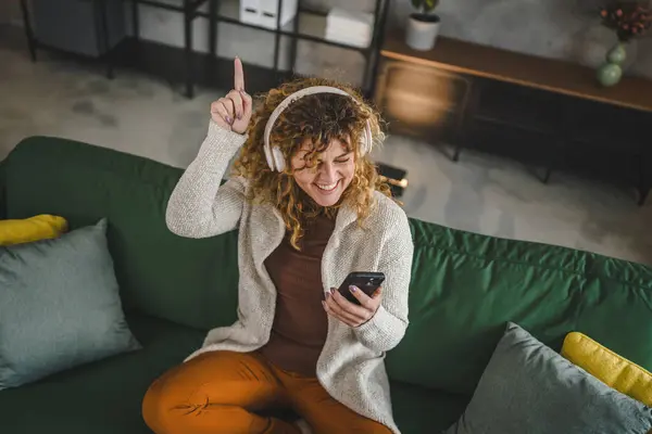 ヘッドフォンを持つ1人の白人女性大人の女性は 音楽を聞くために自宅で携帯電話を使用する オンライン幸せな笑顔歌の喜びは 単独のコピースペースを持っています — ストック写真