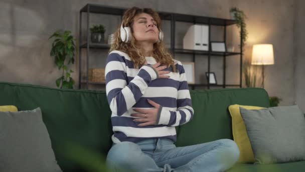1人の女性の大人の慎重な女性ミレニアルオンラインガイド瞑想のためのヘッドフォンを使用してマインドフルネスヨガの目を閉じた本物の人々セルフケアコンセプトのスローモーション — ストック動画