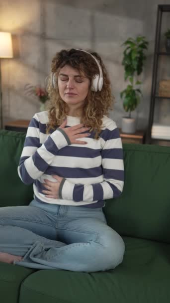 1人の女性の大人の慎重な女性ミレニアルオンラインガイド瞑想のためのヘッドフォンを使用してマインドフルネスヨガの目を閉じた本物の人々セルフケアコンセプトのスローモーション — ストック動画