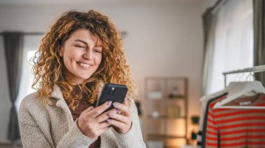 Beyaz saçlı, evde kıvırcık saçlı bir kadın cep telefonu akıllı mesajları kullanıyor. İnternetteki sosyal ağlara mesaj atıyor ya da internette geziniyor.