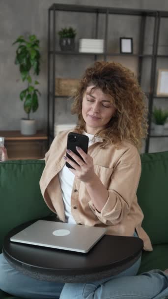 自宅でカーリーヘアを持つ1人の女性は 携帯電話のスマートフォンのSmsテキストを使用したり インターネットのソーシャルネットワークの遅い動きを閲覧します — ストック動画