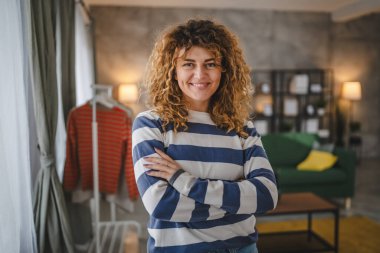 Evde kıvırcık saçlı, mutlu gülümseyen yetişkin beyaz kadın portresi.