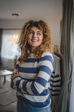 Evde kıvırcık saçlı, mutlu gülümseyen yetişkin beyaz kadın portresi.