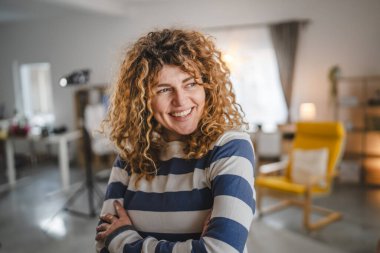 Evde kıvırcık saçlı, mutlu gülümseyen yetişkin beyaz kadın portresi.