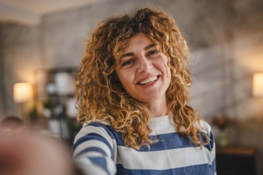 Evde kıvırcık saçlı, yetişkin beyaz bir kadının portresi. Mutlu bir gülümseme. Kendi portresi çirkin kullanıcı tarafından oluşturulmuş.