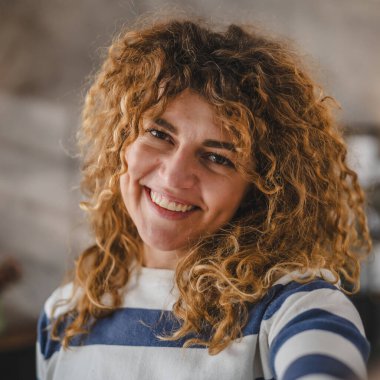 Evde kıvırcık saçlı, yetişkin beyaz bir kadının portresi. Mutlu bir gülümseme. Kendi portresi çirkin kullanıcı tarafından oluşturulmuş.