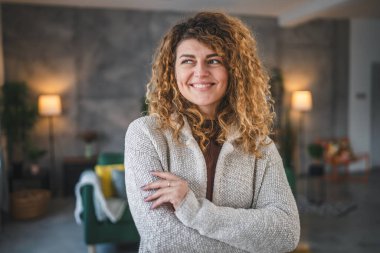Evde kıvırcık saçlı, mutlu gülümseyen yetişkin beyaz kadın portresi.