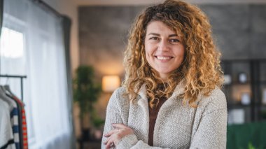 Evde kıvırcık saçlı, mutlu gülümseyen yetişkin beyaz kadın portresi.