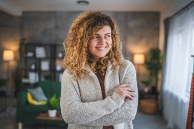 Evde kıvırcık saçlı, mutlu gülümseyen yetişkin beyaz kadın portresi.