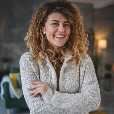 Evde kıvırcık saçlı, mutlu gülümseyen yetişkin beyaz kadın portresi.