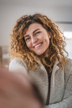 Evde kıvırcık saçlı, yetişkin beyaz bir kadının portresi. Mutlu bir gülümseme. Kendi portresi çirkin kullanıcı tarafından oluşturulmuş.