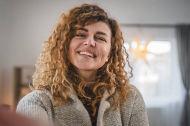 Evde kıvırcık saçlı, yetişkin beyaz bir kadının portresi. Mutlu bir gülümseme. Kendi portresi çirkin kullanıcı tarafından oluşturulmuş.